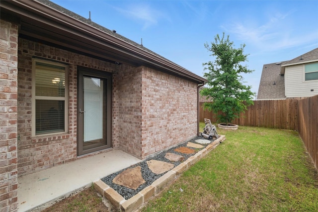 entrance to property featuring fence, a yard, and brick siding