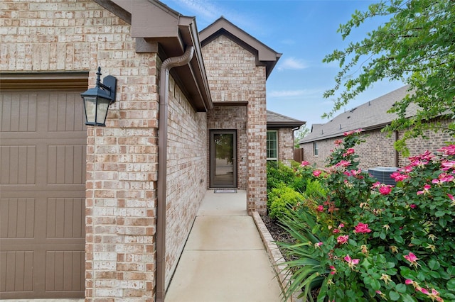 property entrance with an attached garage, central AC, and brick siding