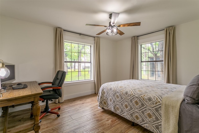 bedroom featuring baseboards, ceiling fan, wood finished floors, and multiple windows