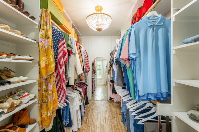 walk in closet featuring an inviting chandelier, arched walkways, and wood finished floors