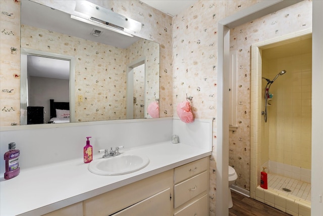 full bathroom featuring vanity, toilet, wallpapered walls, a shower stall, and wood finished floors