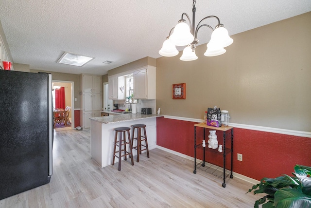 kitchen with freestanding refrigerator, a peninsula, light wood-style floors, a breakfast bar area, and a notable chandelier
