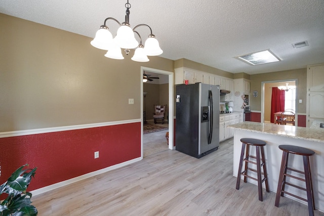 kitchen featuring visible vents, a peninsula, light wood-style floors, stainless steel fridge, and a textured ceiling