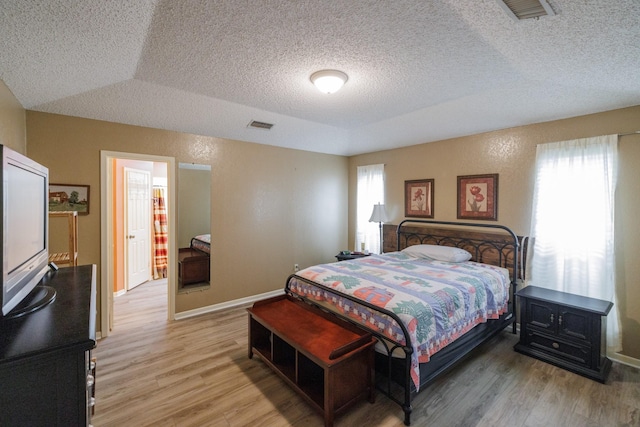 bedroom featuring visible vents, a textured ceiling, light wood-style flooring, and baseboards
