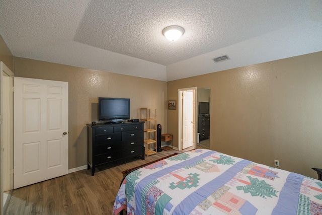 bedroom with a textured ceiling, visible vents, wood finished floors, and vaulted ceiling
