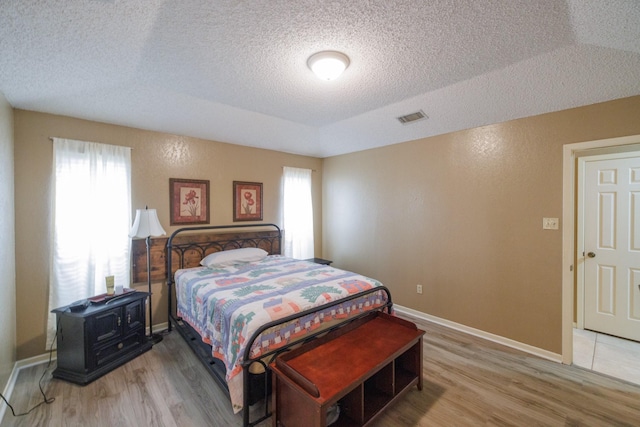 bedroom featuring a textured ceiling, visible vents, baseboards, and light wood finished floors