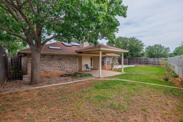 back of property featuring a fenced backyard, brick siding, a patio area, a lawn, and solar panels