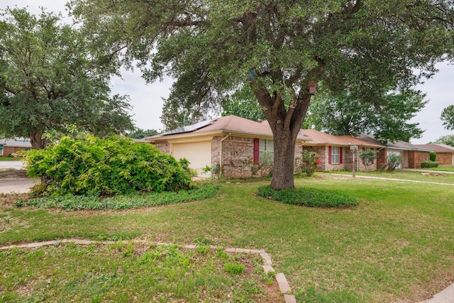 ranch-style house featuring brick siding, solar panels, a front yard, and a garage