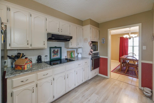 kitchen with white cabinets, a notable chandelier, under cabinet range hood, and black appliances