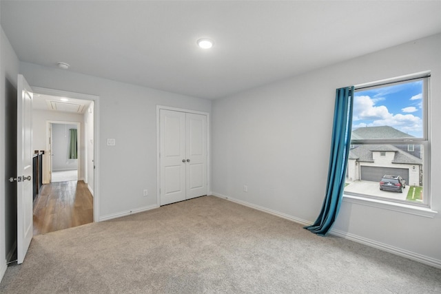 unfurnished bedroom with a closet, baseboards, carpet, and attic access