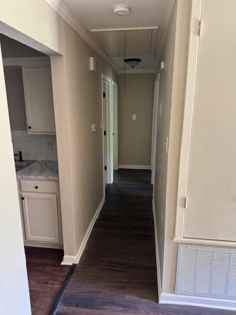 corridor with ornamental molding, attic access, baseboards, visible vents, and dark wood-style floors