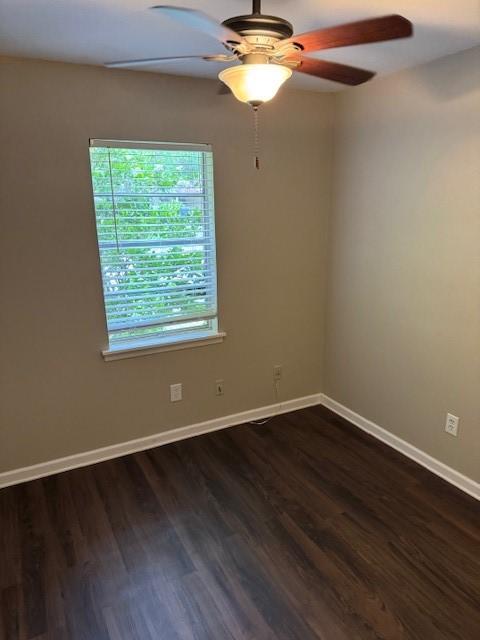 unfurnished room with a ceiling fan, baseboards, and dark wood-type flooring