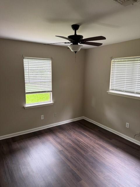unfurnished room with baseboards, ceiling fan, visible vents, and dark wood-type flooring