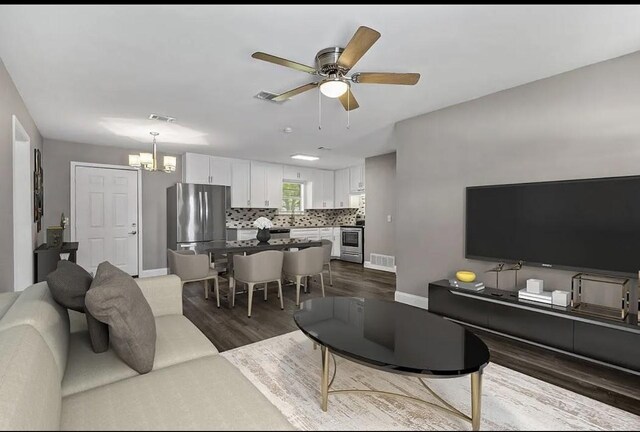 living room featuring baseboards, visible vents, ceiling fan with notable chandelier, and dark wood-type flooring