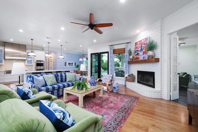 living room with crown molding, a brick fireplace, wood finished floors, recessed lighting, and a ceiling fan