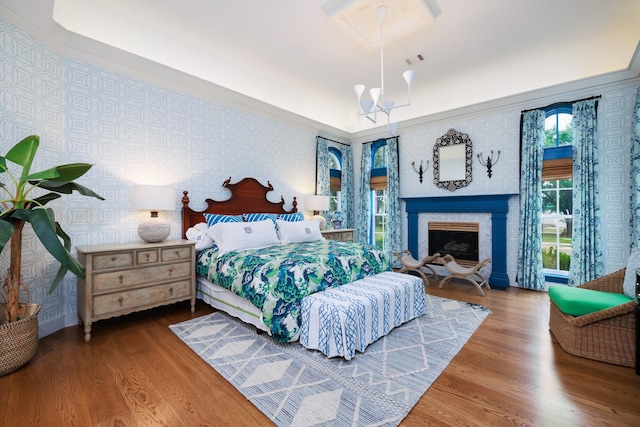 bedroom featuring a notable chandelier, a fireplace, wallpapered walls, wood finished floors, and visible vents