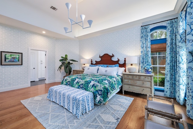 bedroom featuring wood finished floors, wallpapered walls, a chandelier, and visible vents