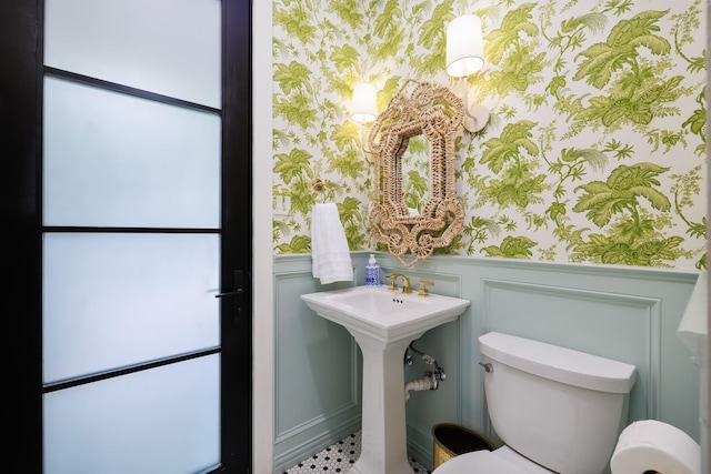 half bathroom featuring a wainscoted wall, toilet, and wallpapered walls