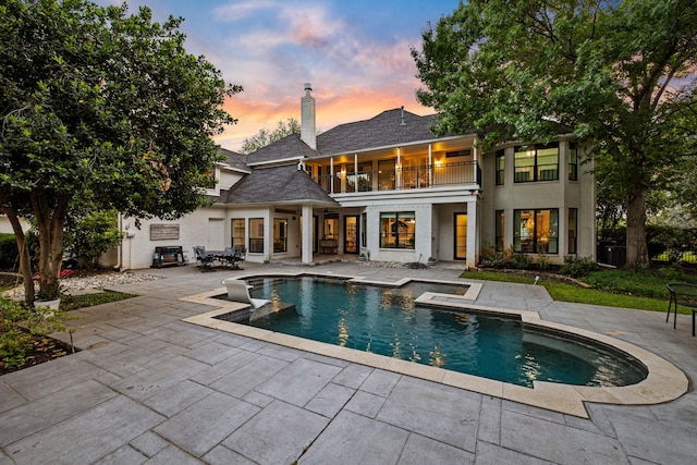 rear view of property featuring a chimney, a balcony, a patio area, and an outdoor pool