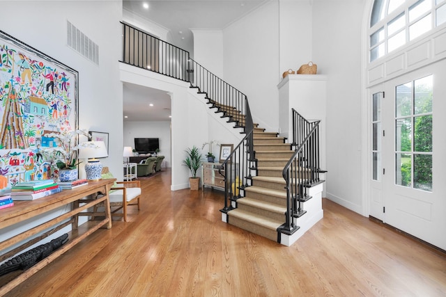 foyer featuring a high ceiling, baseboards, wood finished floors, visible vents, and stairway