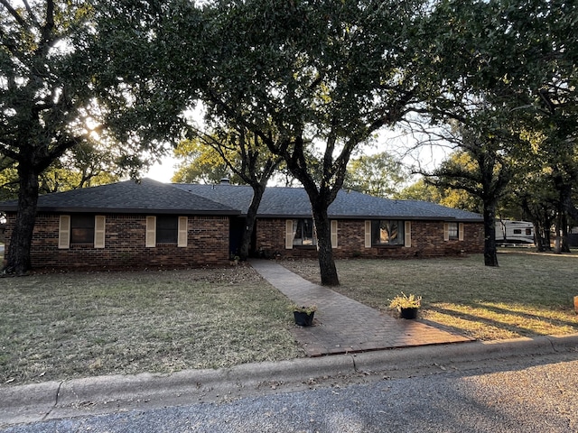 single story home featuring brick siding, a shingled roof, and a front lawn