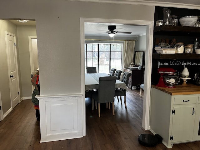 dining space with dark wood-type flooring, ornamental molding, baseboards, and a ceiling fan