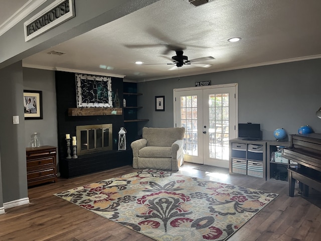 living area featuring ornamental molding, wood finished floors, a large fireplace, french doors, and a ceiling fan