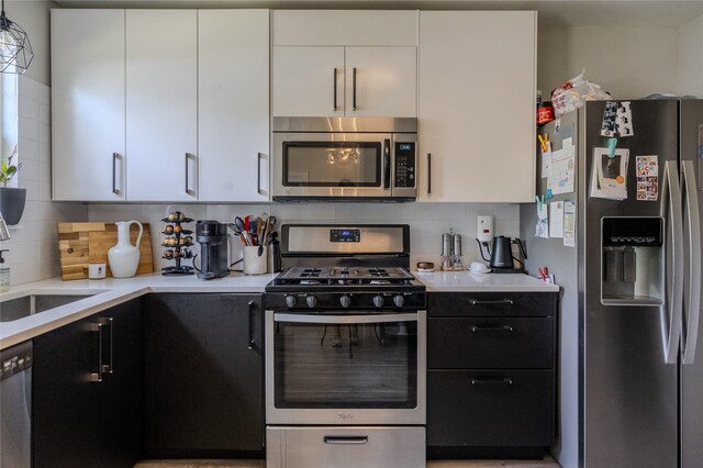 kitchen featuring light countertops, white cabinets, tasteful backsplash, dark cabinets, and appliances with stainless steel finishes