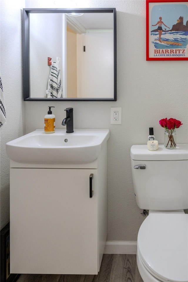 half bathroom featuring vanity, baseboards, toilet, and wood finished floors