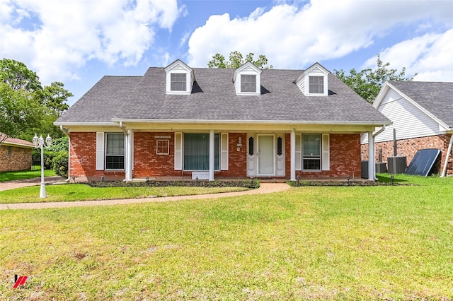 new england style home with a porch, central AC, a shingled roof, and a front yard
