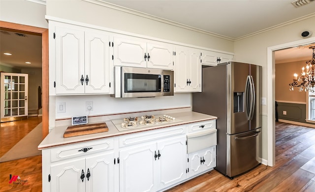 kitchen featuring crown molding, white cabinetry, appliances with stainless steel finishes, and an inviting chandelier