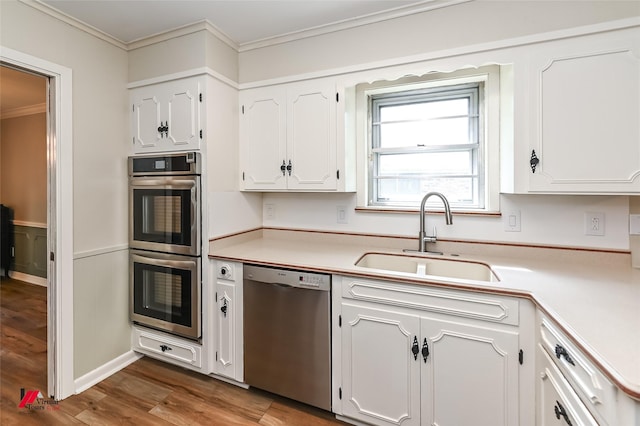 kitchen with appliances with stainless steel finishes, a sink, white cabinetry, wood finished floors, and ornamental molding
