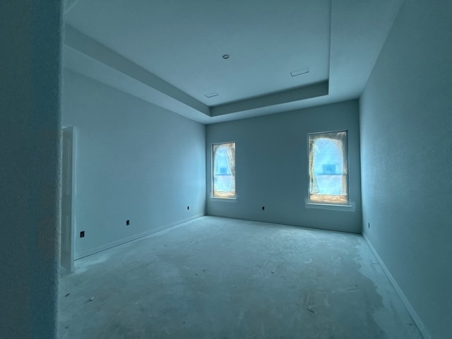 unfurnished room featuring unfinished concrete floors, baseboards, and a tray ceiling