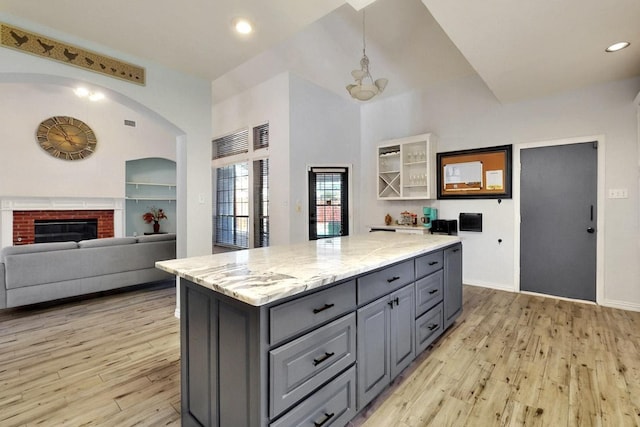 3017 Holford Rd, Richardson, TX 75082 - kitchen with gray cabinets, light wood-style flooring, a kitchen island, a fireplace, and light stone countertops