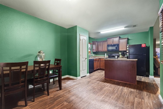 kitchen featuring baseboards, dark wood-style floors, a center island, light countertops, and black appliances