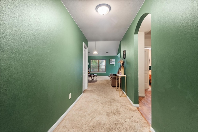 corridor featuring arched walkways, baseboards, carpet, and a textured wall