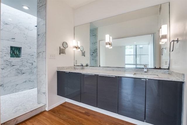 bathroom featuring a sink, a marble finish shower, double vanity, and wood finished floors