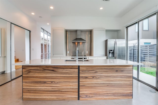 kitchen featuring light countertops, wall chimney exhaust hood, concrete floors, and stainless steel fridge with ice dispenser