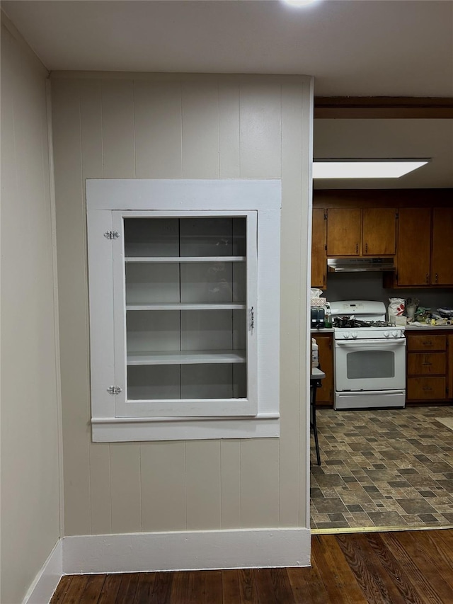 kitchen with under cabinet range hood, white gas stove, baseboards, and dark wood-type flooring