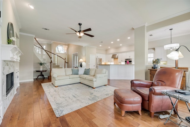 living room with a ceiling fan, visible vents, light wood-type flooring, a tile fireplace, and stairs