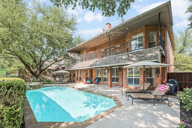 rear view of property featuring a chimney, a patio area, brick siding, a fenced backyard, and a balcony