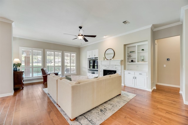 living area with visible vents, crown molding, a fireplace, ceiling fan, and light wood-style flooring
