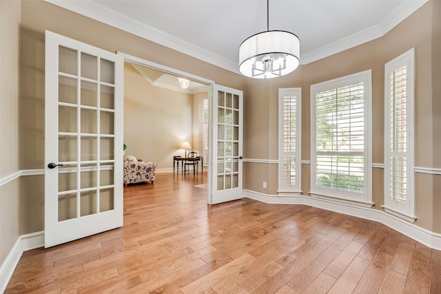 unfurnished dining area with french doors, baseboards, a chandelier, ornamental molding, and light wood-style flooring