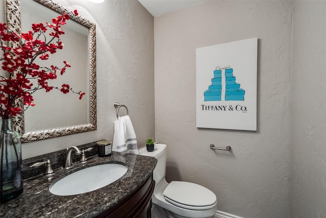 half bathroom featuring toilet, a textured wall, and vanity