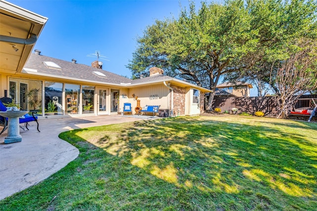 rear view of property featuring fence, brick siding, a chimney, a lawn, and a patio