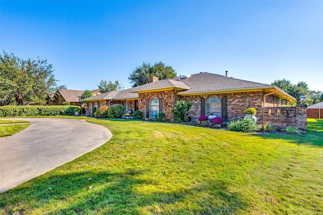 single story home featuring brick siding, curved driveway, a chimney, and a front yard