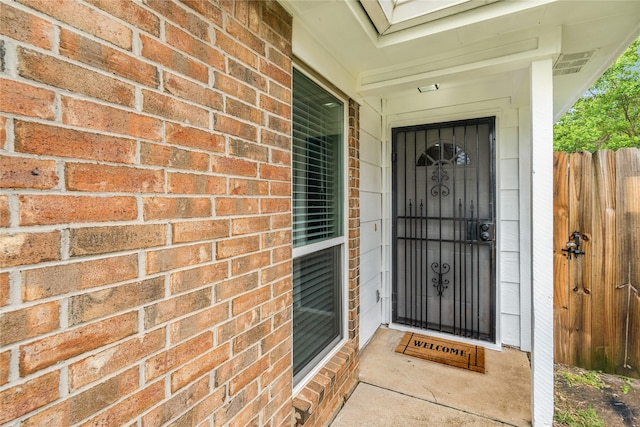 property entrance with brick siding, visible vents, and fence
