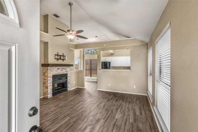 unfurnished living room featuring visible vents, a stone fireplace, ceiling fan, dark wood finished floors, and vaulted ceiling