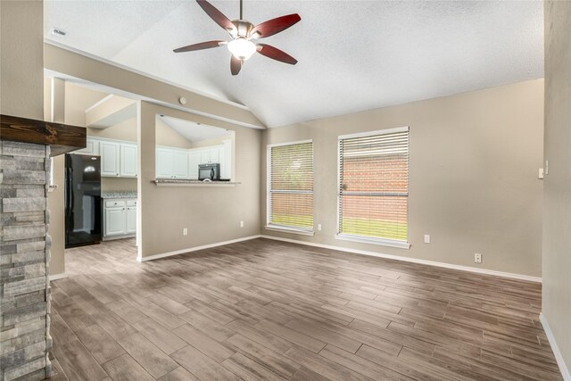 unfurnished living room featuring a textured ceiling, a ceiling fan, baseboards, wood finished floors, and vaulted ceiling