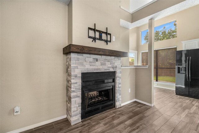 unfurnished living room featuring a stone fireplace, baseboards, a towering ceiling, and wood finished floors